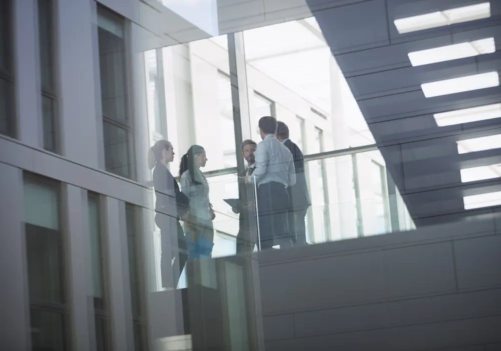 Senior European executives meeting on a glass walkway inside a modern Amsterdam office building - the kind of Netherlands and European workplaces Go Ahead HiRe partners with on senior recruitment